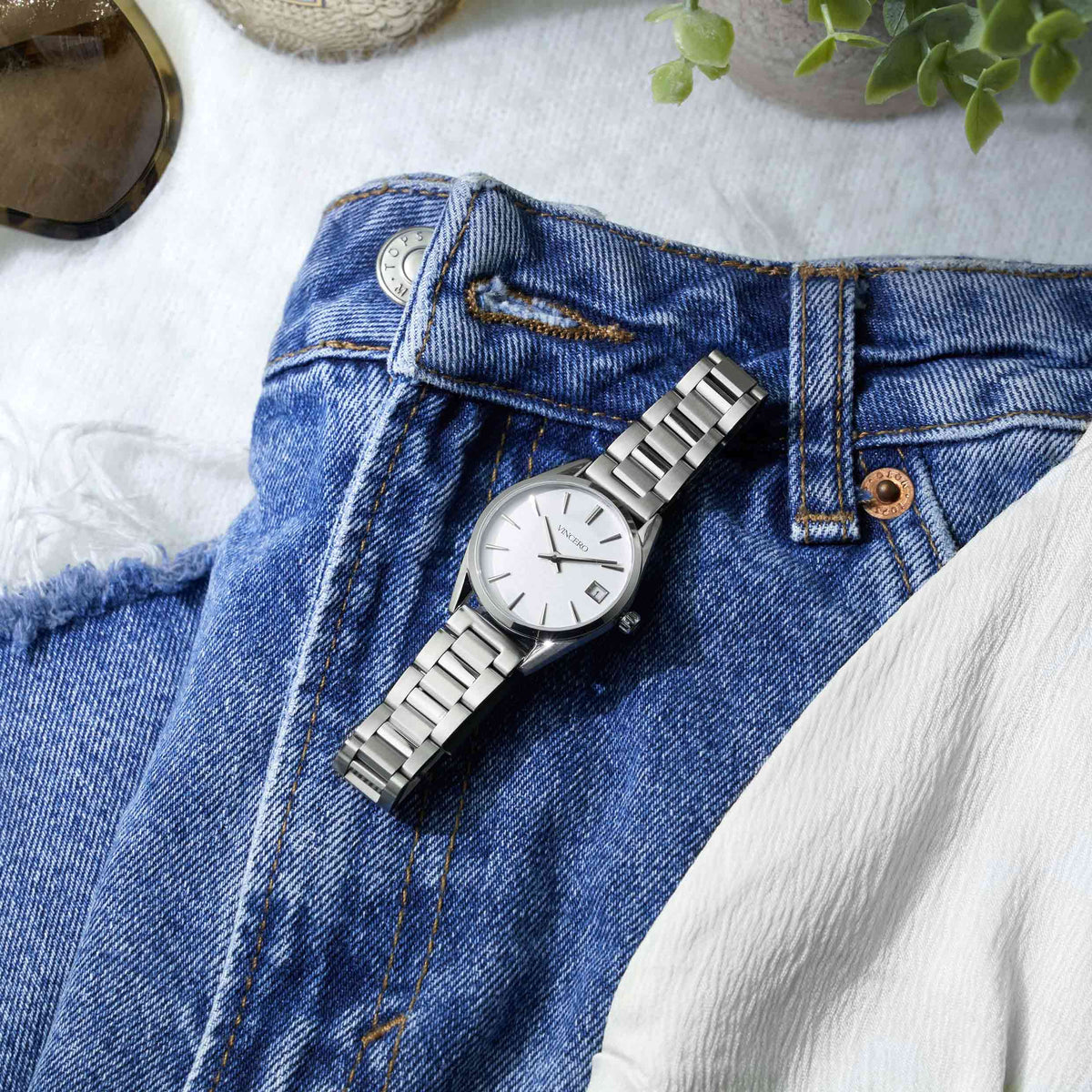 Silver watch on a pair of blue jeans with a white fabric background