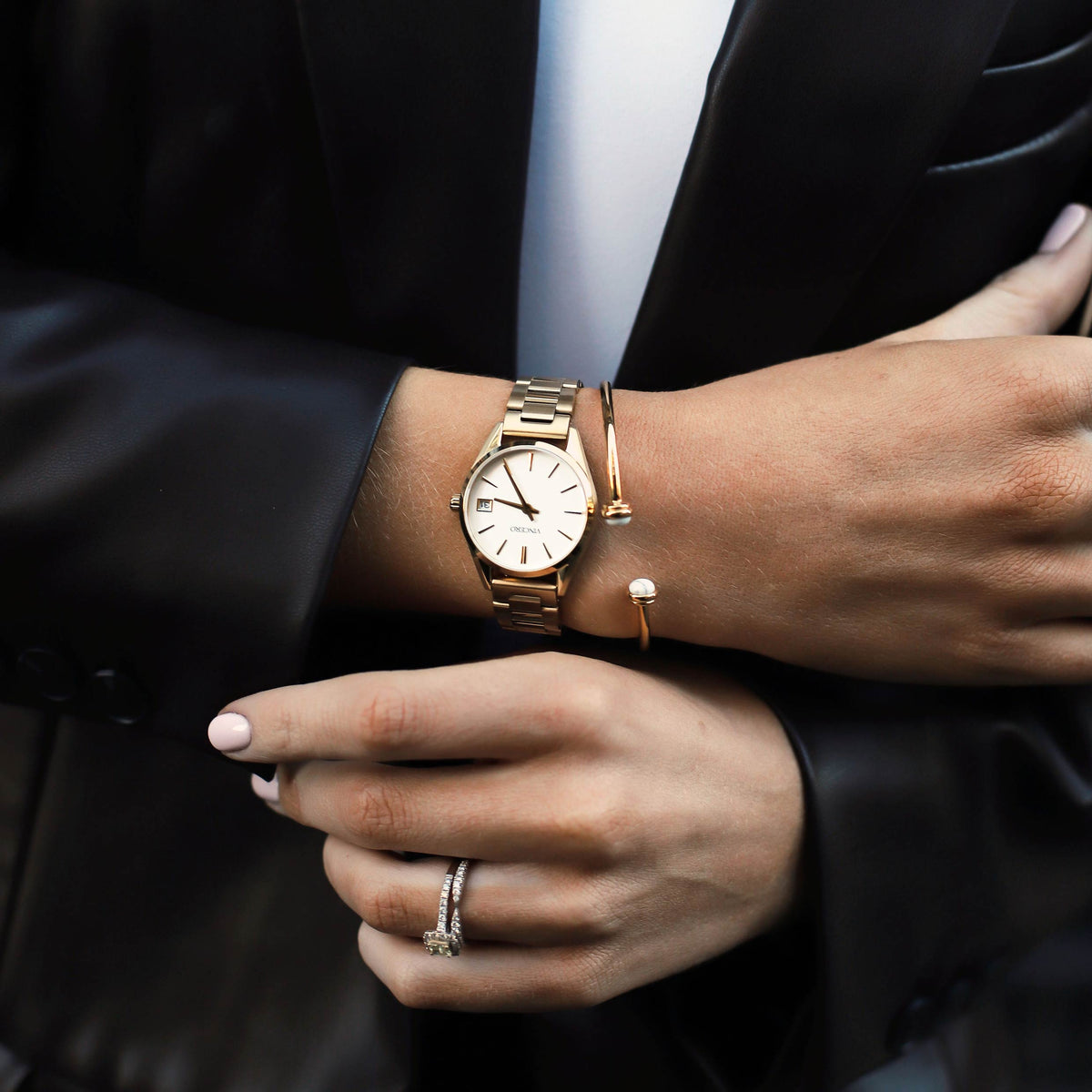Close-up of a person's wrist wearing a gold watch and bracelet, with a black background.