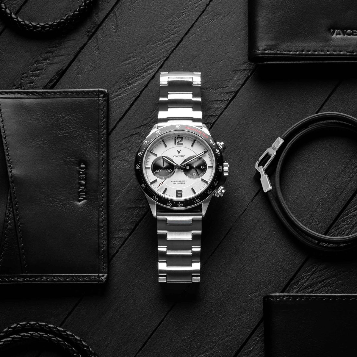 Silver watch with black and white face on a dark wooden surface with leather items.