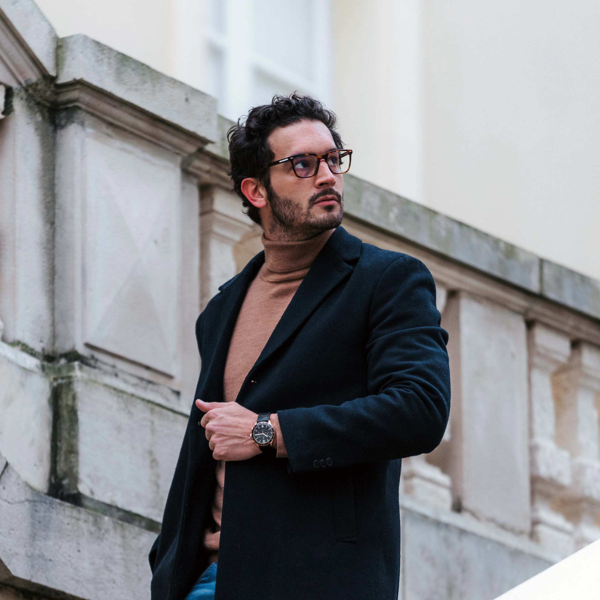 Man wearing a dark coat with a building in the background