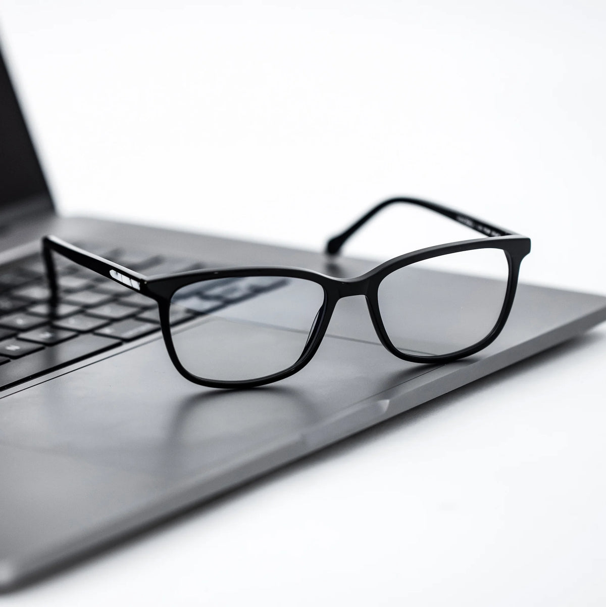 Black eyeglasses on a laptop keyboard with a white background