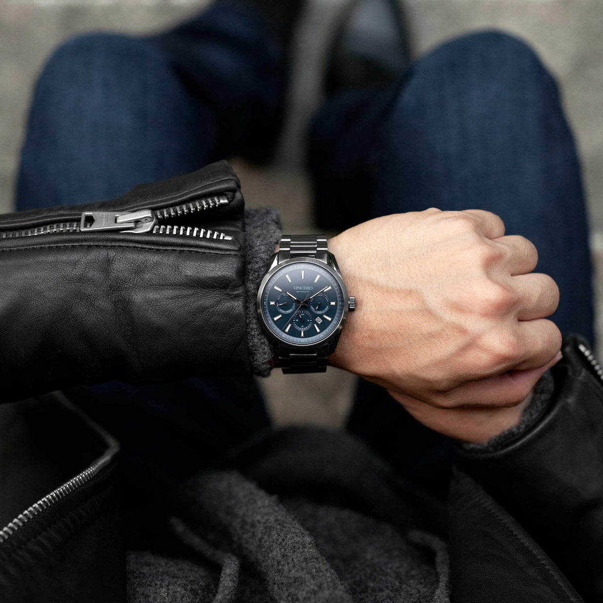 Person wearing a black leather jacket and a watch on a blurred background
