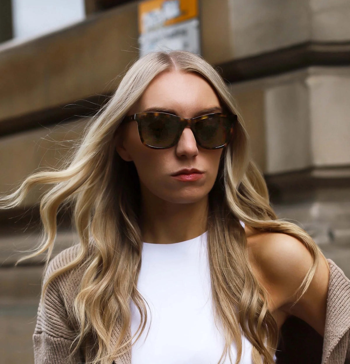 Woman wearing sunglasses and a beige cardigan in an urban setting