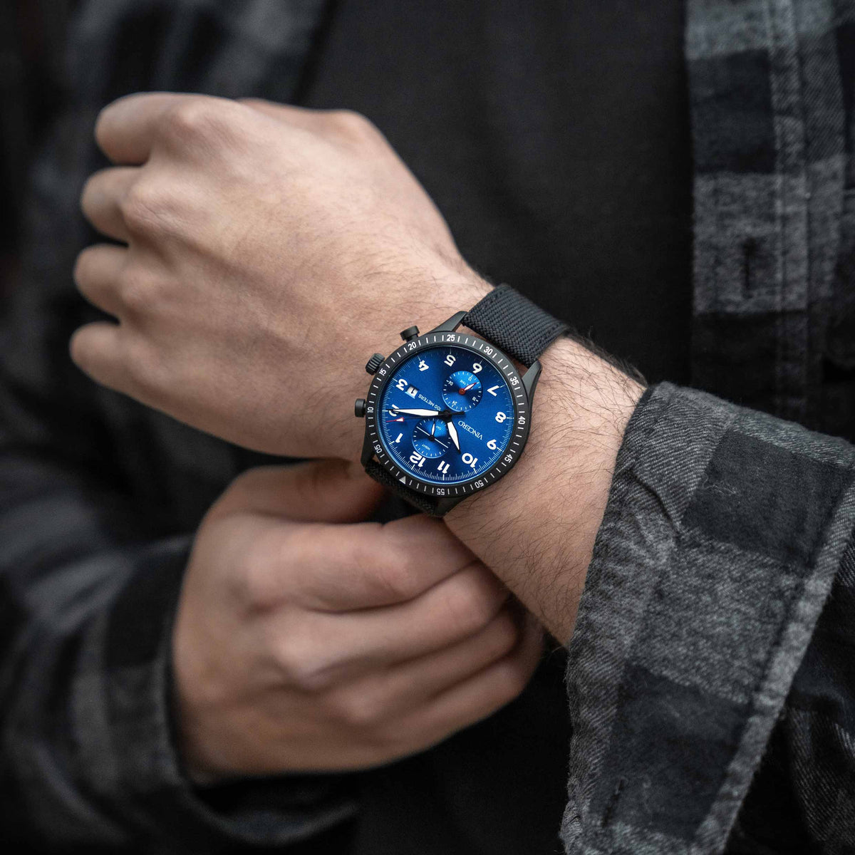 Person wearing a black watch with a blue face on a dark background