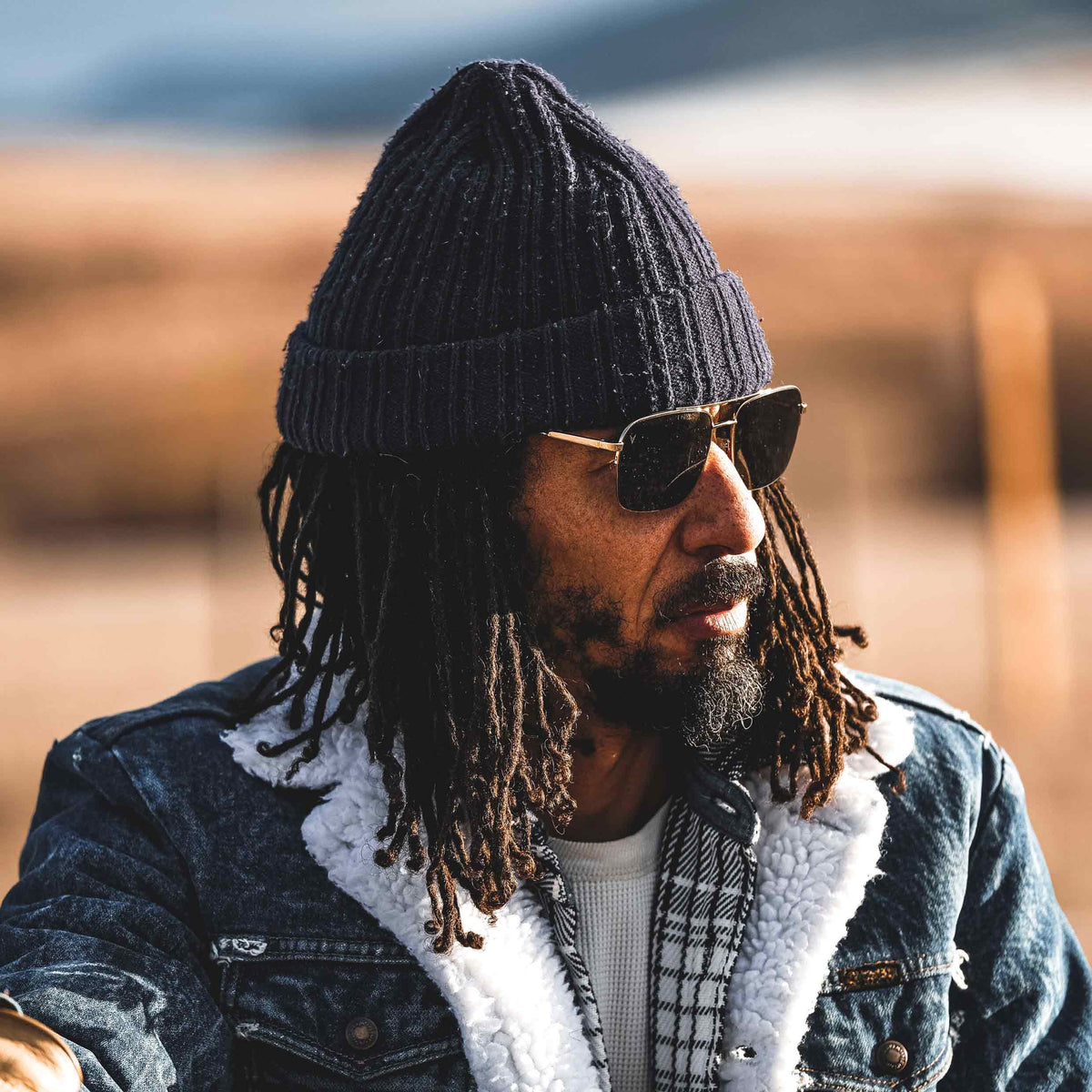 Man wearing a black knit beanie and sunglasses with a blurred background