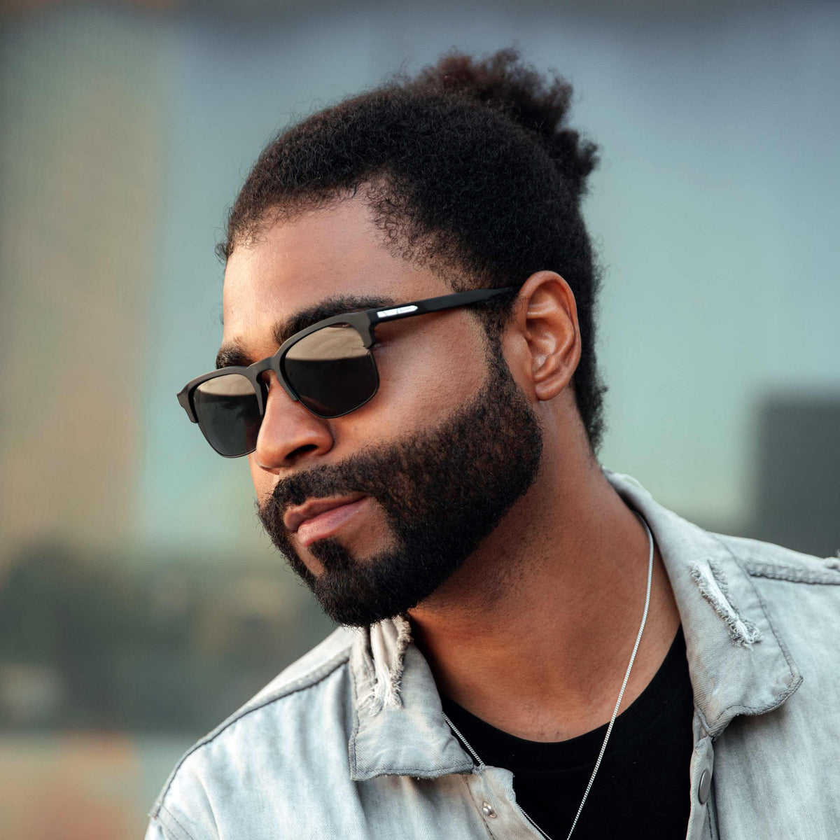 Man wearing sunglasses and a light jacket with a blurred background