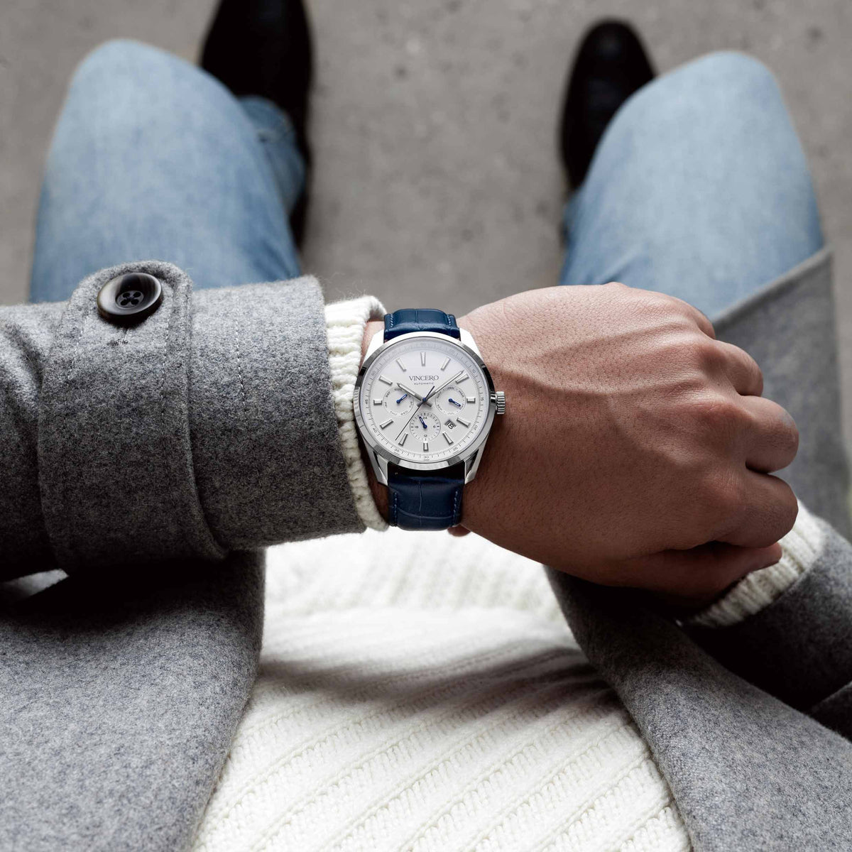 Person wearing a watch with a blue strap and gray coat on a neutral background