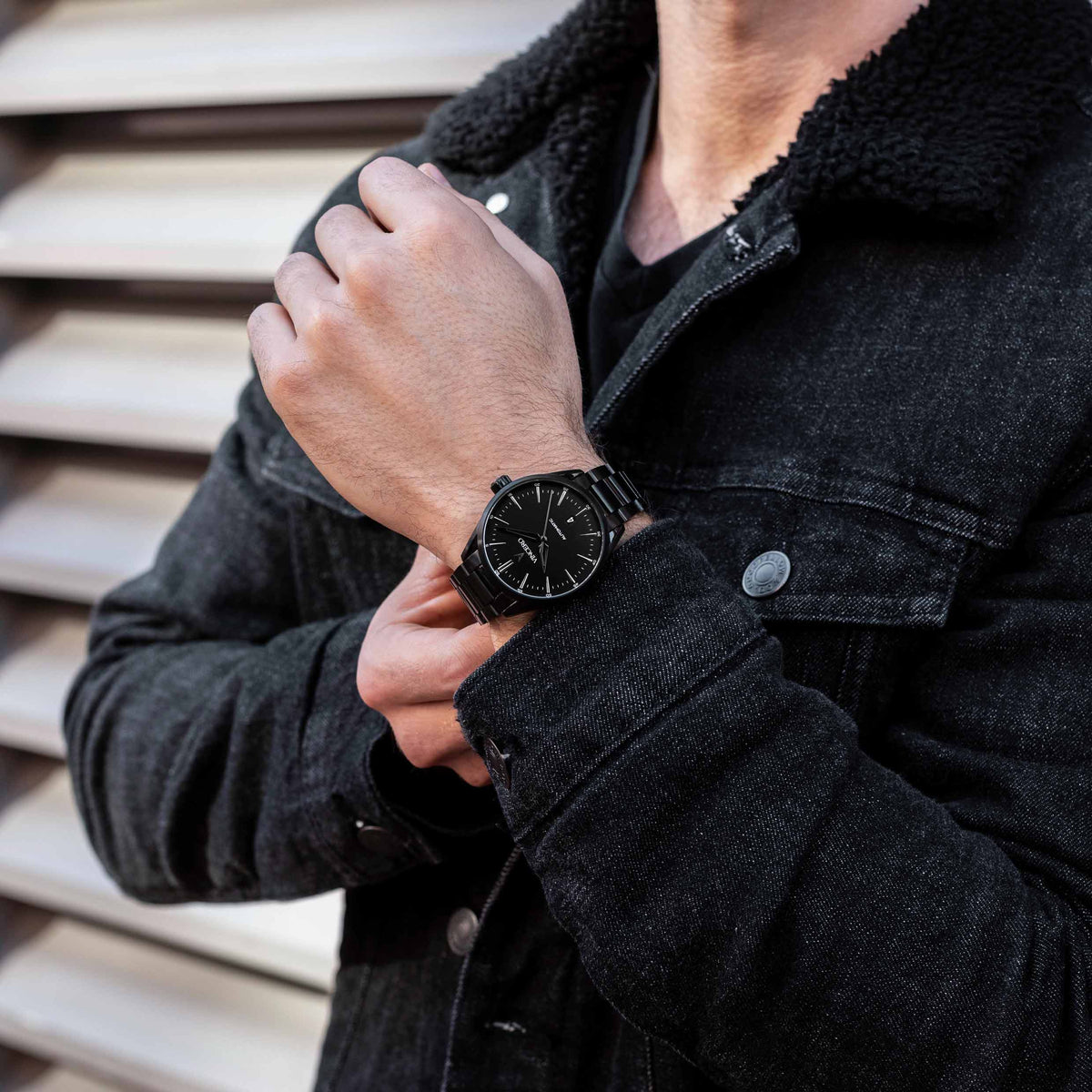 Person wearing a black coat and black watch, adjusting their jacket.