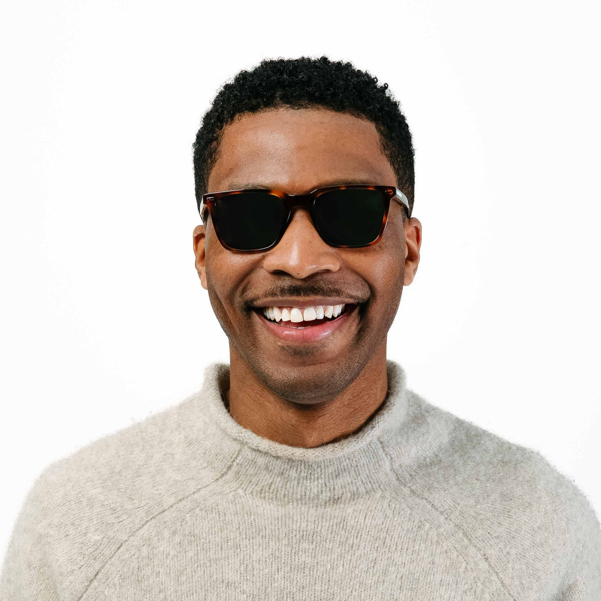 Man wearing sunglasses and a light gray sweater on a white background