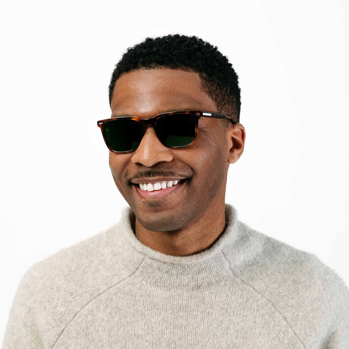 Man wearing sunglasses and a light gray sweater on a white background