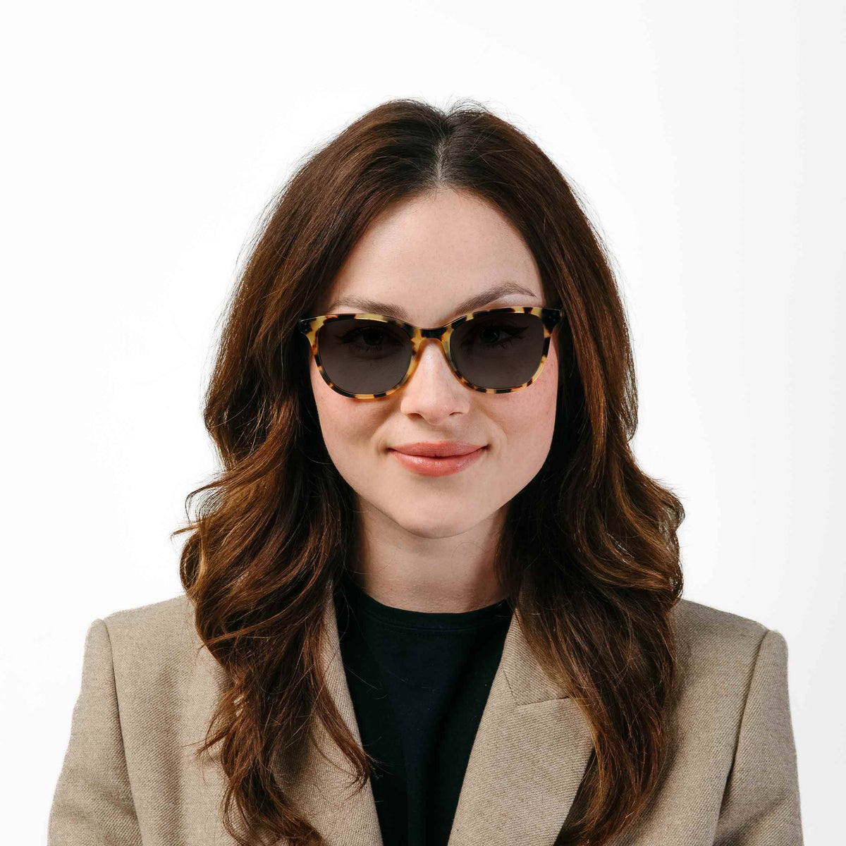 Woman wearing sunglasses and a beige blazer on a white background
