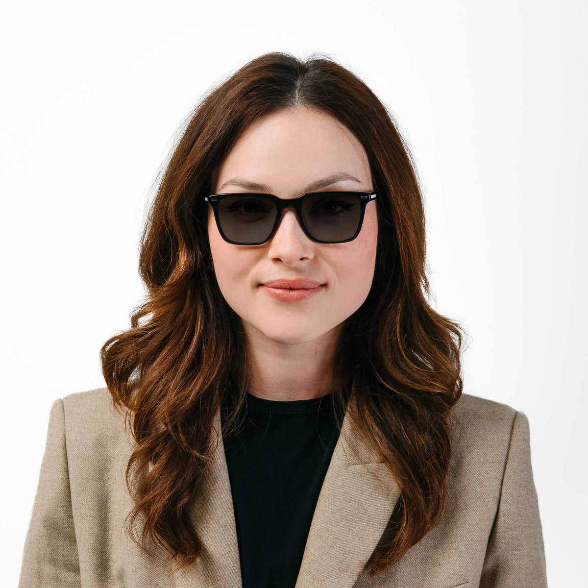 Woman wearing sunglasses and a beige blazer on a white background