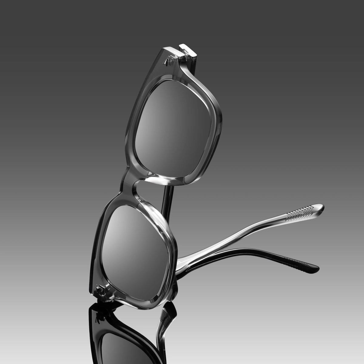 Silver sunglasses on a reflective surface with a gradient gray background