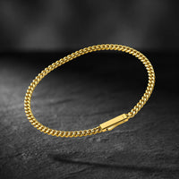 A gold-toned metal chain bracelet with a rectangular clasp, displayed on a dark textured surface.