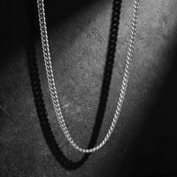 A silver-toned metal chain necklace draped in a U-shape against a dark textured background, with dramatic shadow casting along the chain.