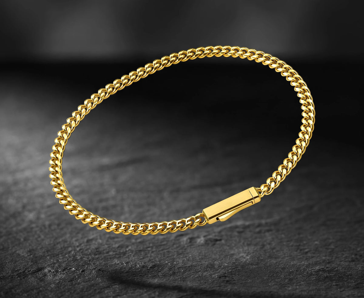 A polished yellow gold curb link bracelet with a rectangular slide clasp, displayed on a dark textured slate surface.