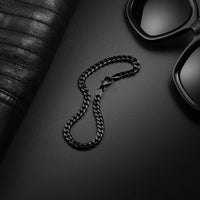 Black chain necklace on a dark surface with sunglasses and leather items.