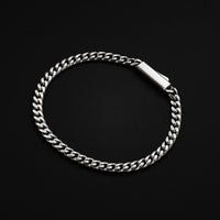 A silver-toned Cuban link chain bracelet with a polished rectangular clasp, displayed on a solid black background.