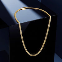 A gold-toned chain necklace draped over a glossy black display block against a dark blue studio background.