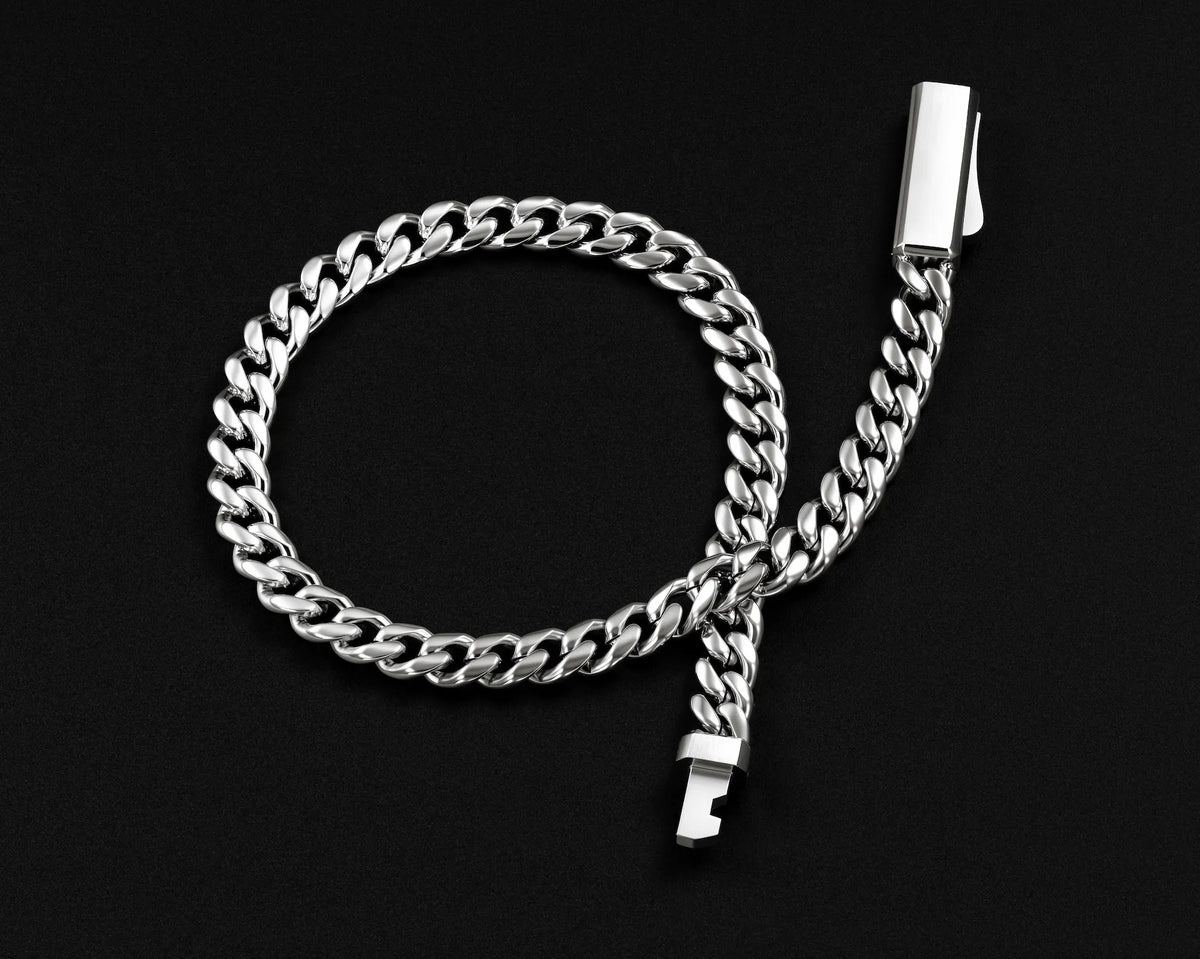 A silver-toned Cuban link chain accessory with a rectangular metal clip and a small metal tag, arranged on a solid black background.