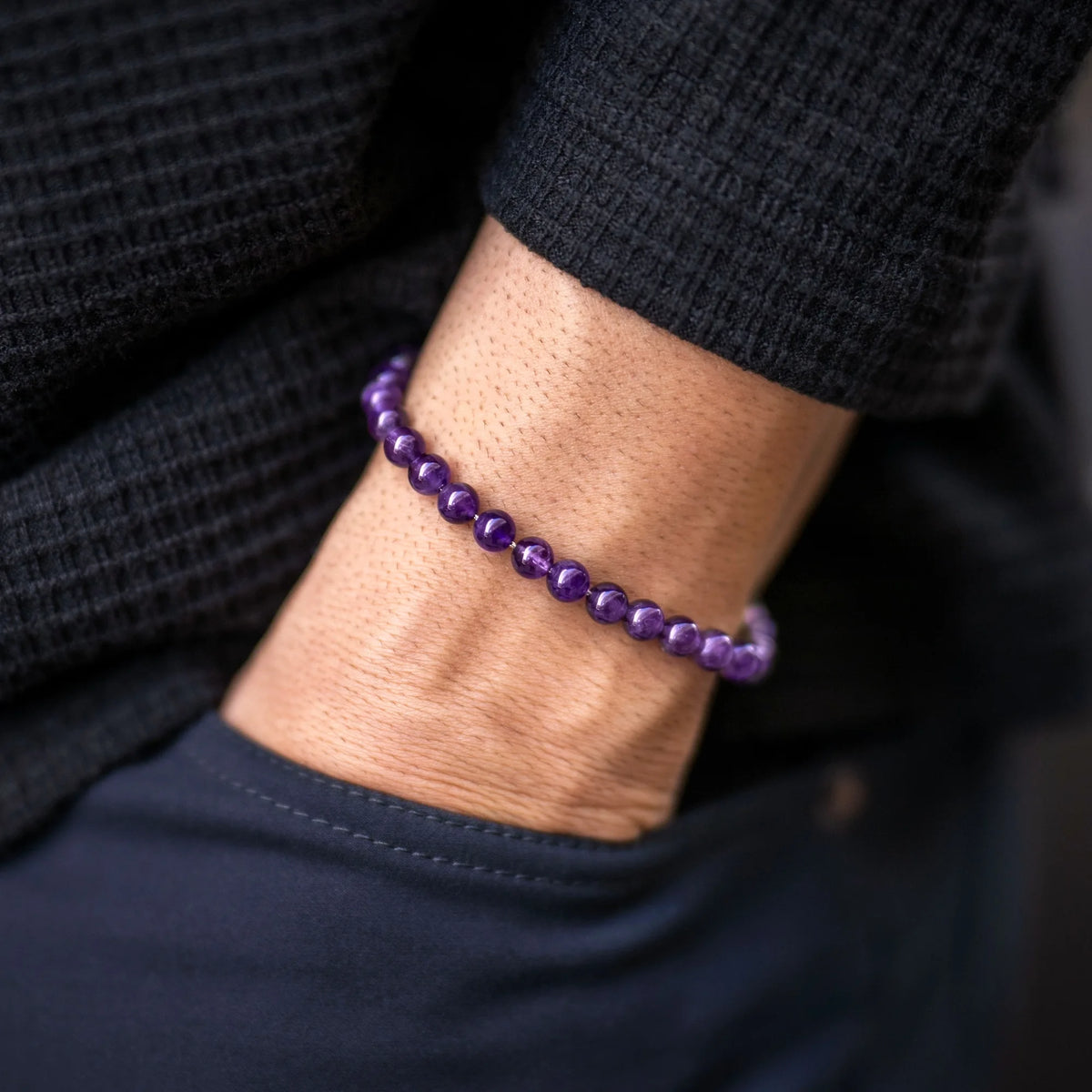 Purple beaded bracelet on a wrist with a dark background