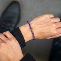 Person wearing a purple beaded bracelet on a blurred background