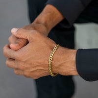 A close-up of a person's hands clasped together, wearing a thick gold Cuban link chain bracelet on one wrist.