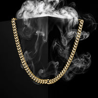 A thick gold-toned curb chain necklace draped in an inverted U shape over a black background with dramatic white smoke swirling around it.