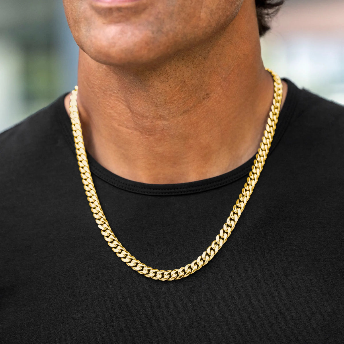 A close-up of a man wearing a thick, shiny gold Cuban link chain necklace over a black t-shirt.