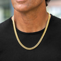 A close-up of a man wearing a thick, shiny gold Cuban link chain necklace over a black t-shirt.