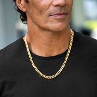 A close-up of a man wearing a thick gold Cuban link chain necklace over a black t-shirt.