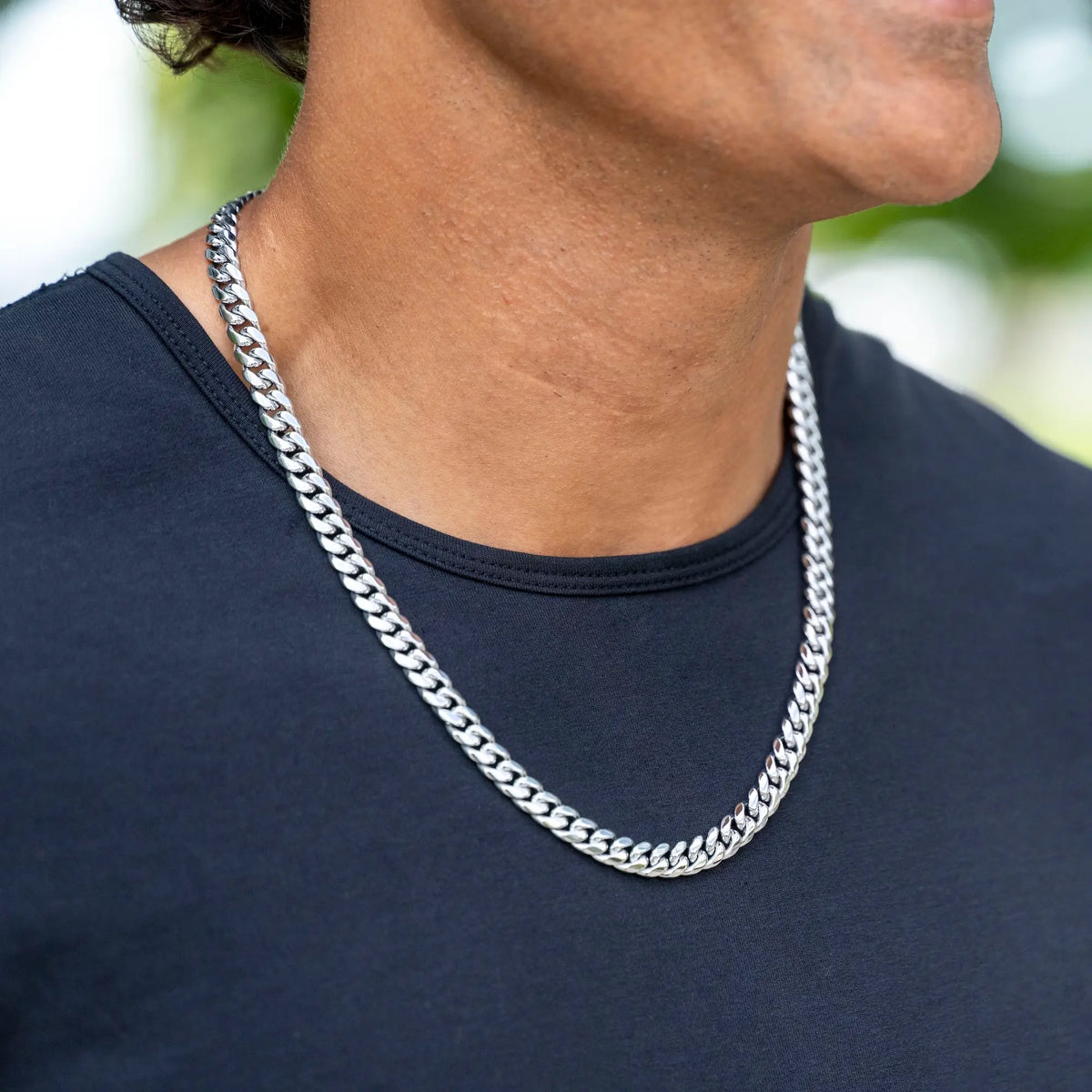 A close-up of a person wearing a thick silver Cuban link chain necklace over a black t-shirt.