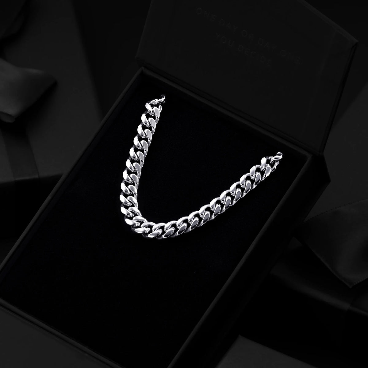 A silver-toned Cuban link chain necklace displayed inside an open black presentation box on a black velvet insert.