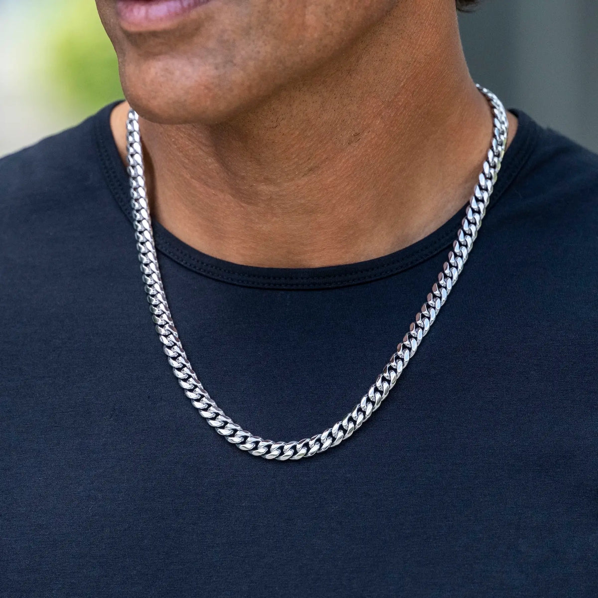 A close-up of a man wearing a thick silver Cuban link chain necklace over a black t-shirt.