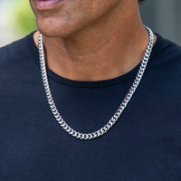 A close-up of a man wearing a thick silver Cuban link chain necklace over a black t-shirt.