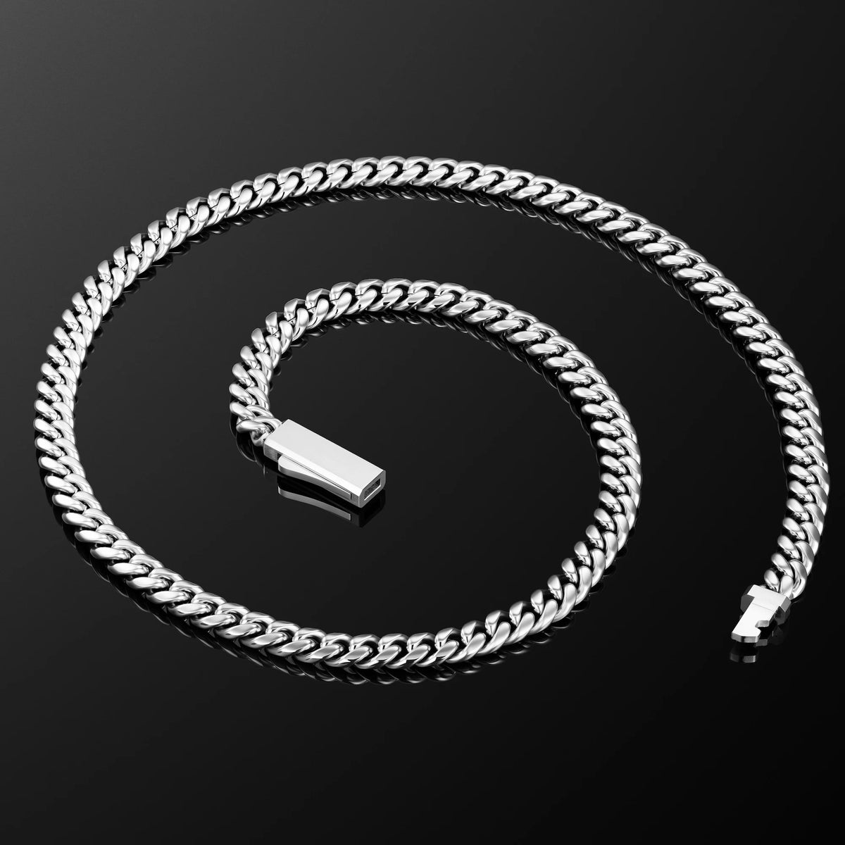 A silver-toned Cuban link chain necklace coiled on a reflective black surface, with a polished rectangular clasp visible near the center.
