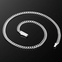 A silver-toned Cuban link chain necklace coiled on a reflective black surface, with a polished rectangular clasp visible near the center.