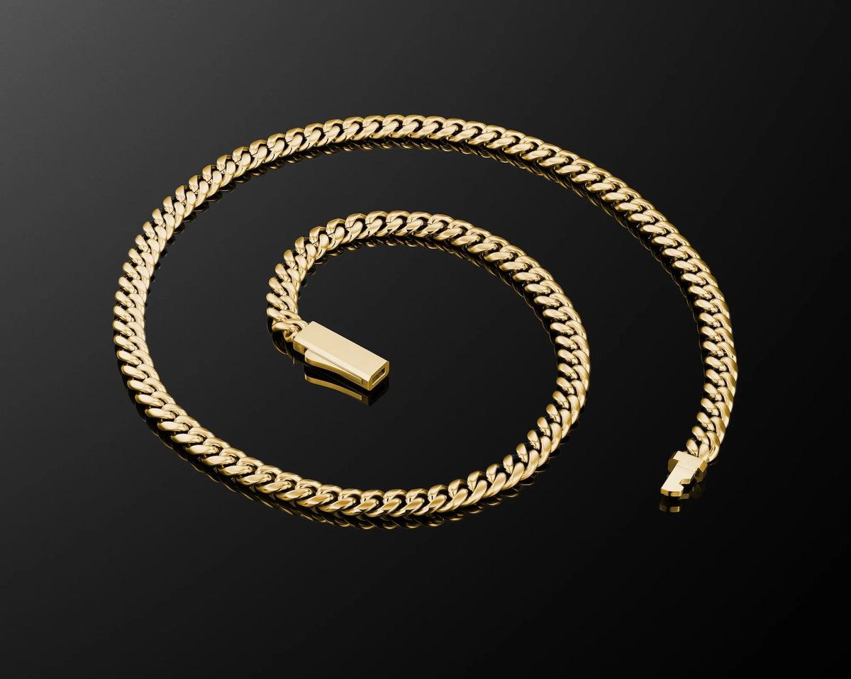 A gold Cuban link chain necklace with a polished rectangular tag, arranged in a spiral on a reflective black surface.