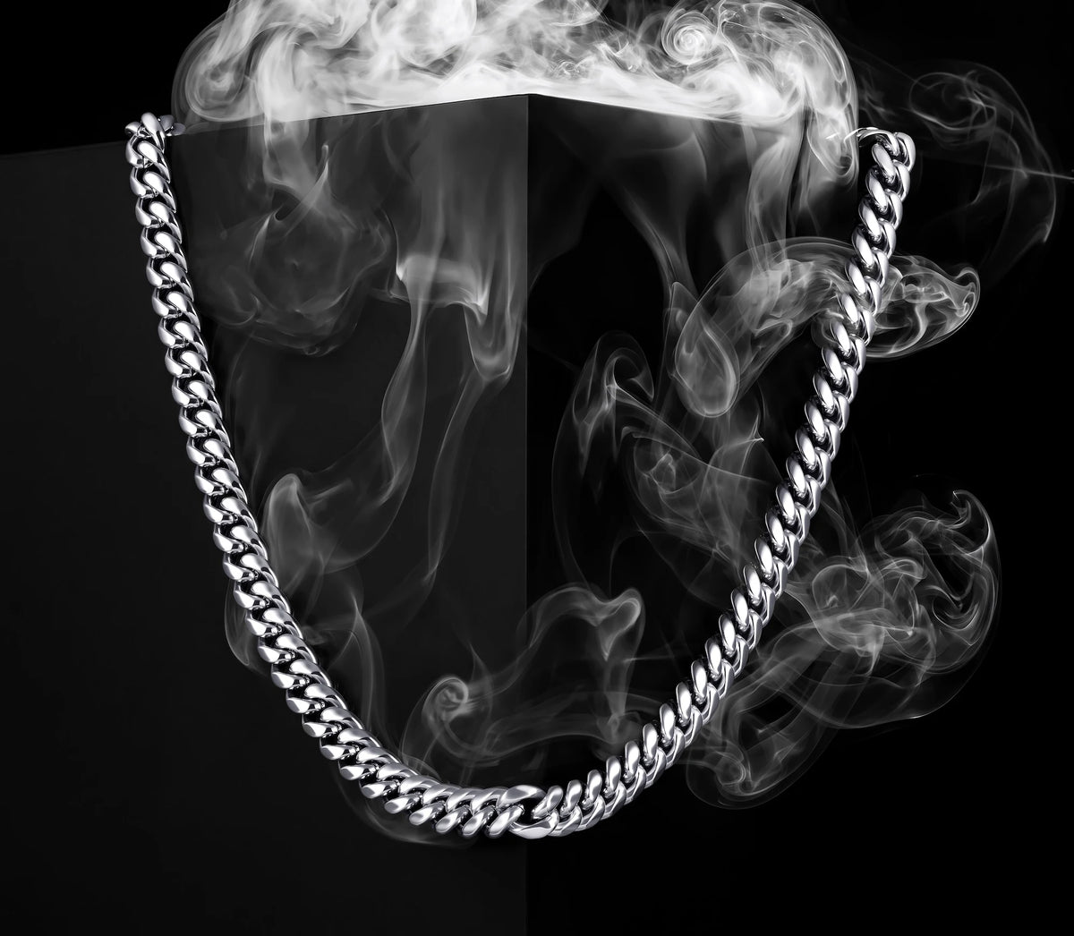 A chunky silver-tone metal chain necklace draped in an arch, set against a black background with dramatic white smoke effects.