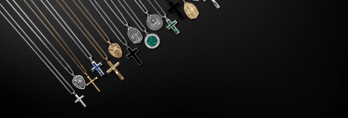 A row of assorted jewelry pendants on chains, including crosses, medallions, and oval charms in silver, gold, green, and black, arranged diagonally on a solid black background.
