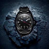A black analog watch with a matching black metal bracelet, featuring a textured black dial with white and red accents, presented in a dramatic scene that appears to burst through a dark, cracked stone surface.