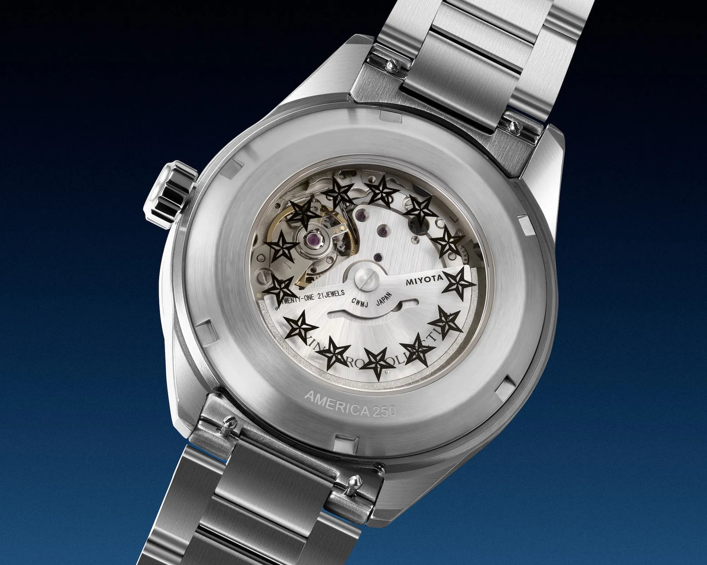 Close-up of a stainless steel wristwatch showing the open back and transparent dial with visible Miyota movement and star-shaped markers, set against a dark blue gradient background.