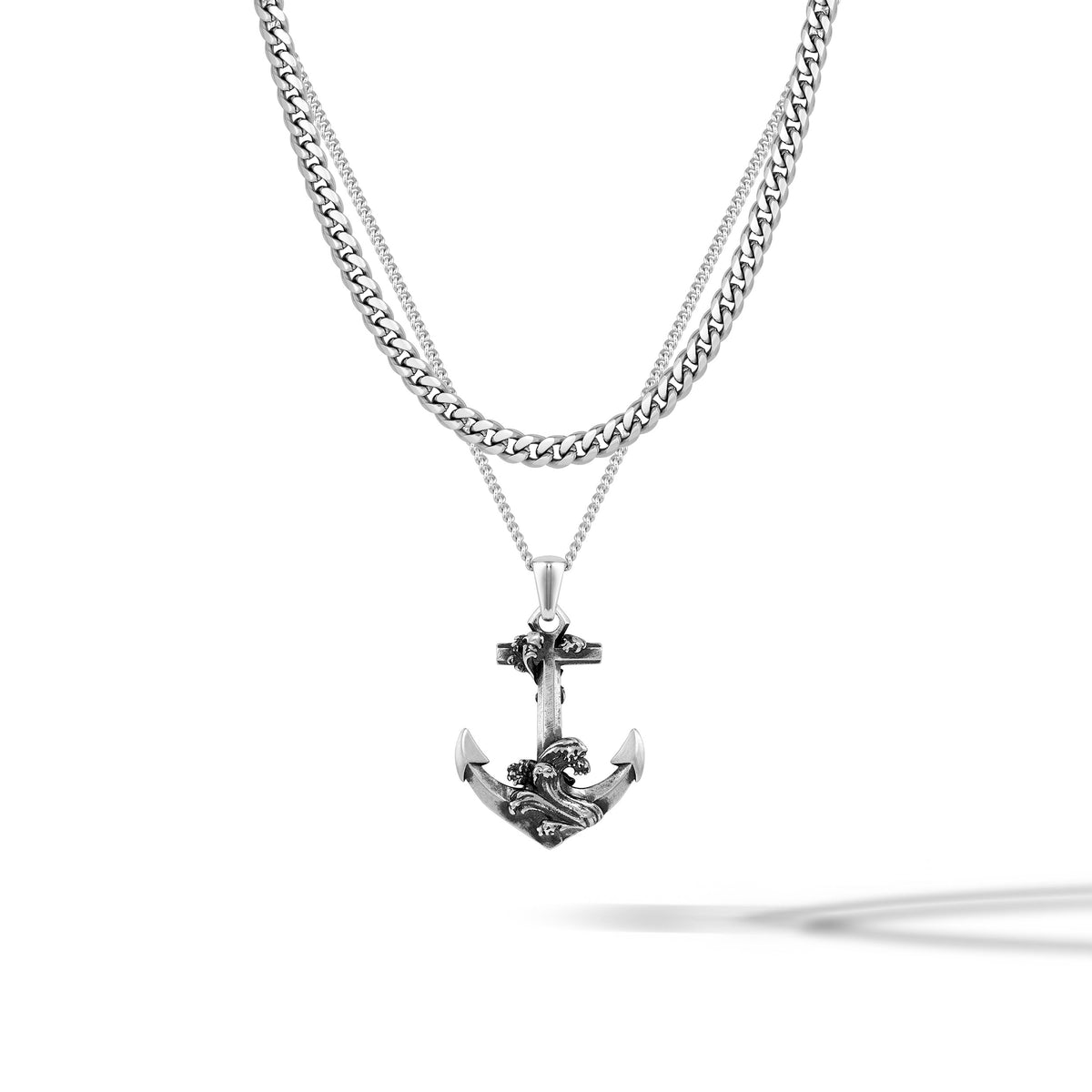 A silver-toned double-strand necklace featuring a thick curb chain and a delicate chain with an anchor pendant, displayed on a clean white background with a soft shadow.