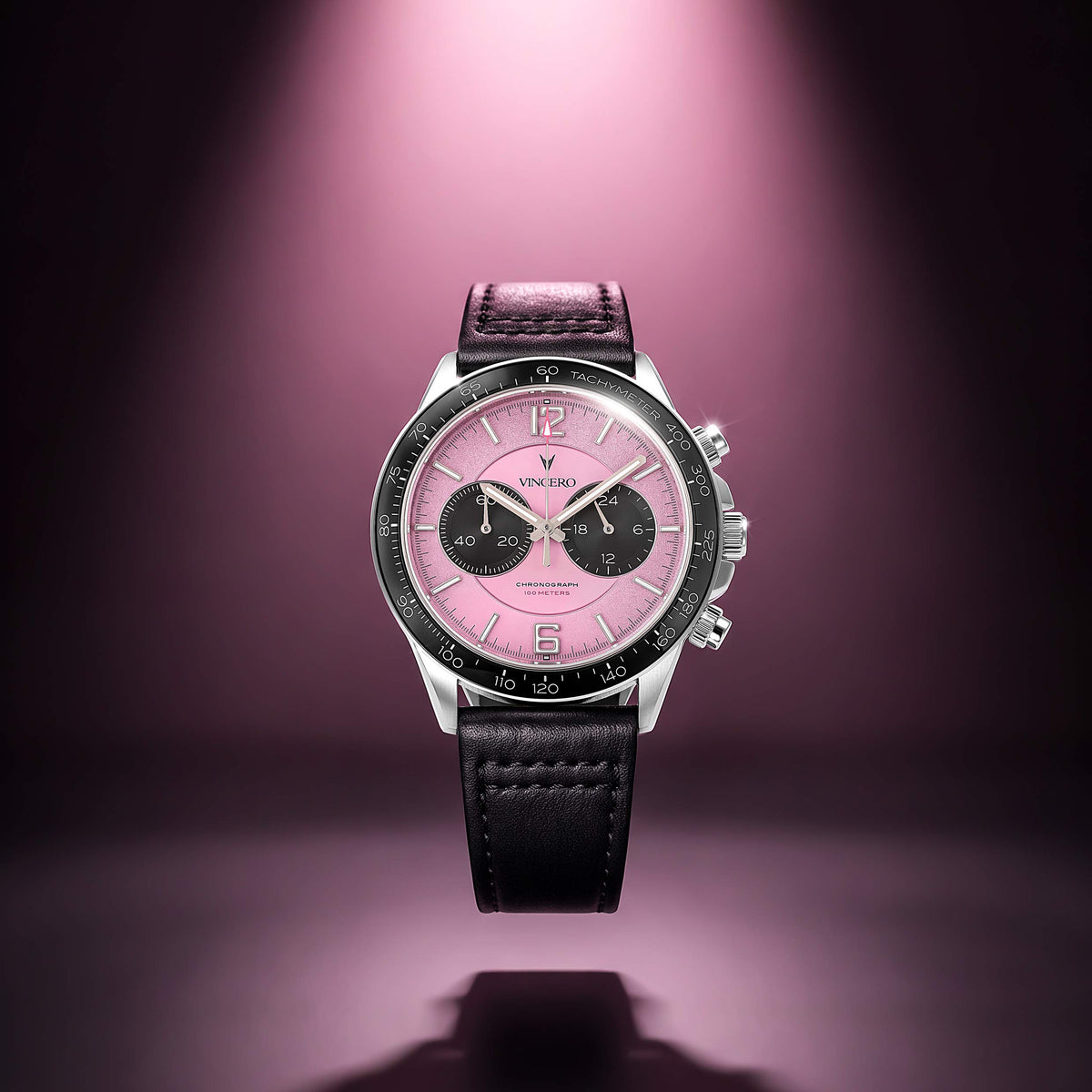 A luxury chronograph watch by Vincero, featuring a pink dial, black subdials, a black leather strap, and a silver-tone case, centered against a dark purple background with a spotlight effect.