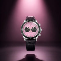 A luxury chronograph watch by Vincero, featuring a pink dial, black subdials, a black leather strap, and a silver-tone case, centered against a dark purple background with a spotlight effect.