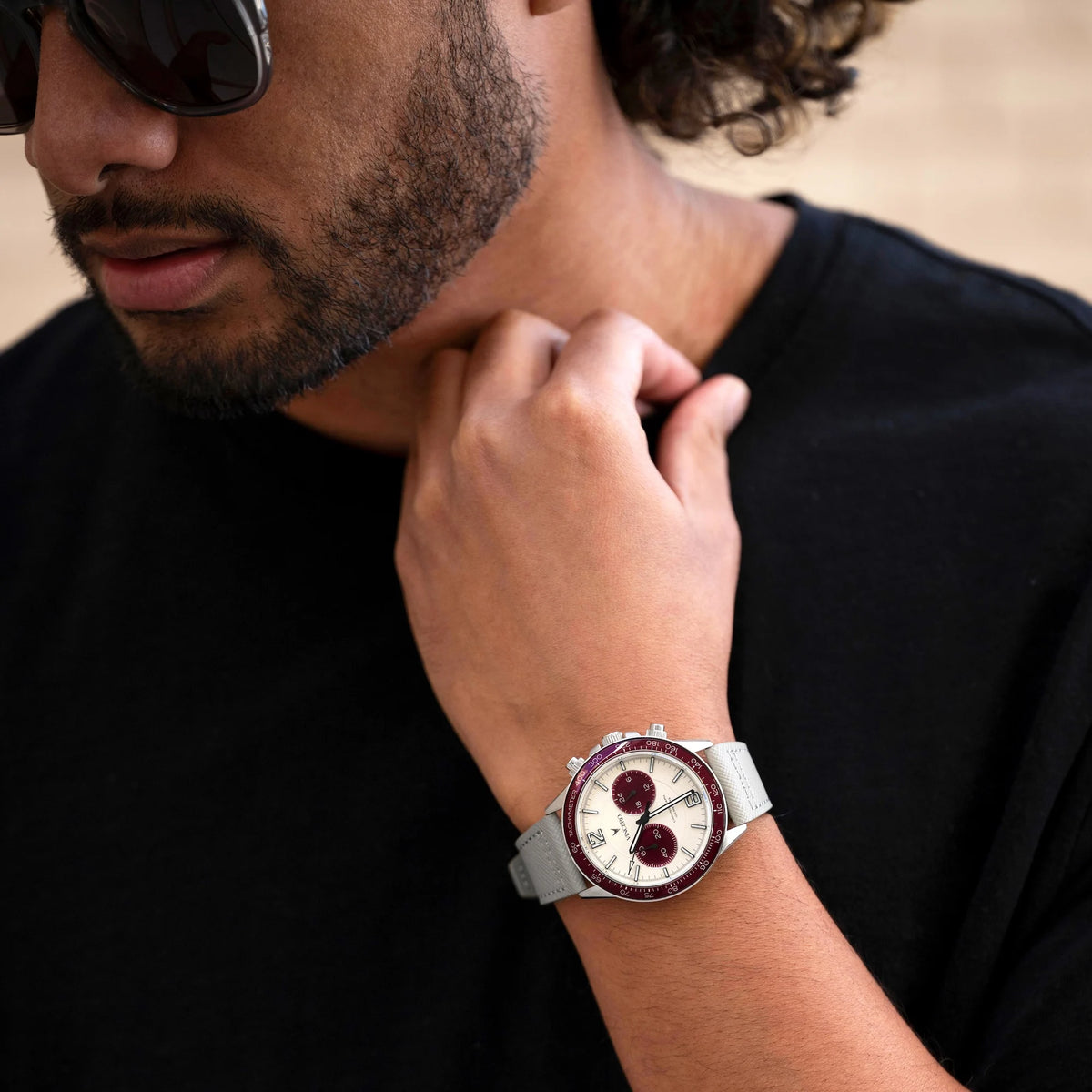 Man wearing a watch with a black shirt and sunglasses, close-up of wrist and face.