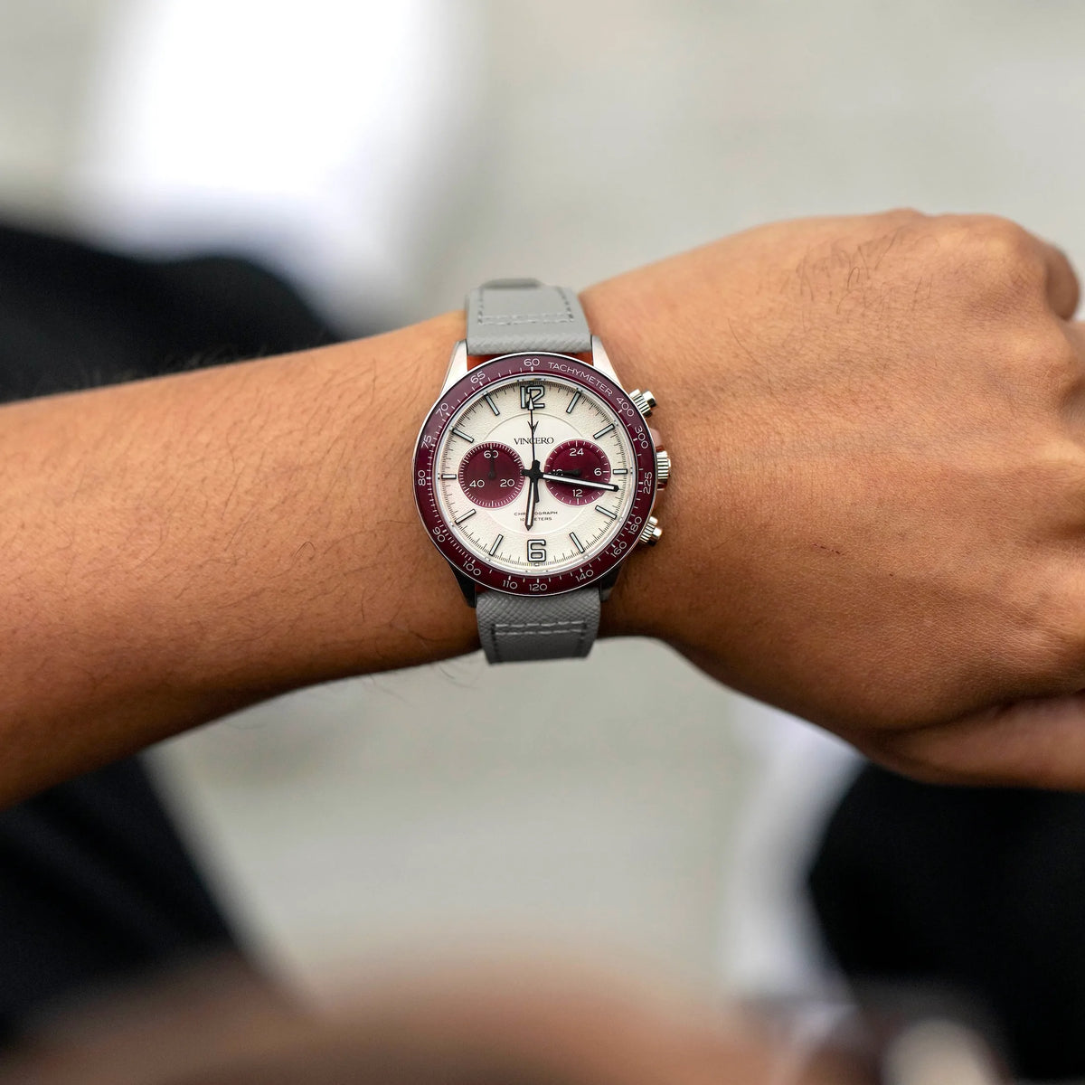 Wrist wearing a watch with a maroon face on a blurred background