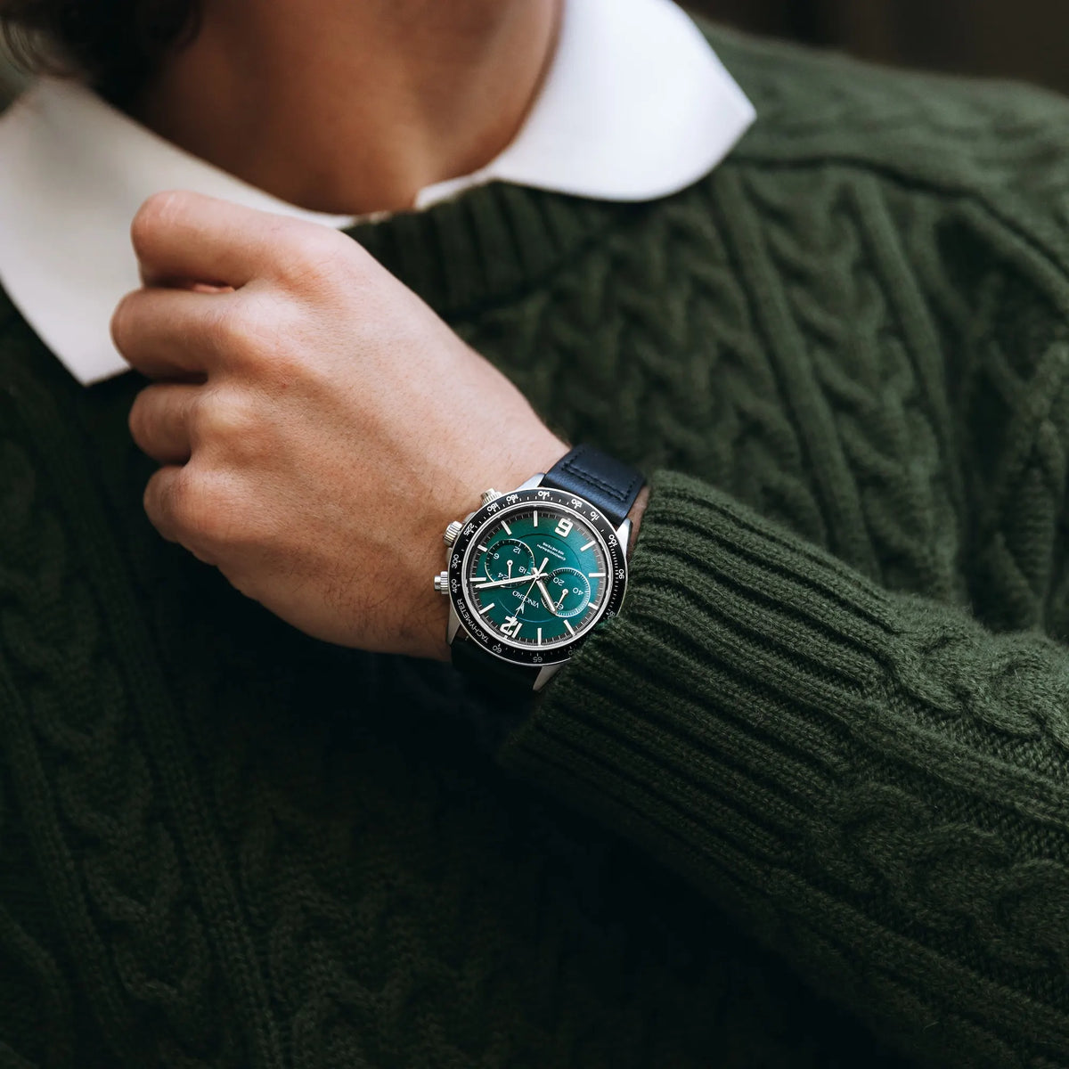 Person wearing a dark green cable-knit sweater with a watch on their wrist.