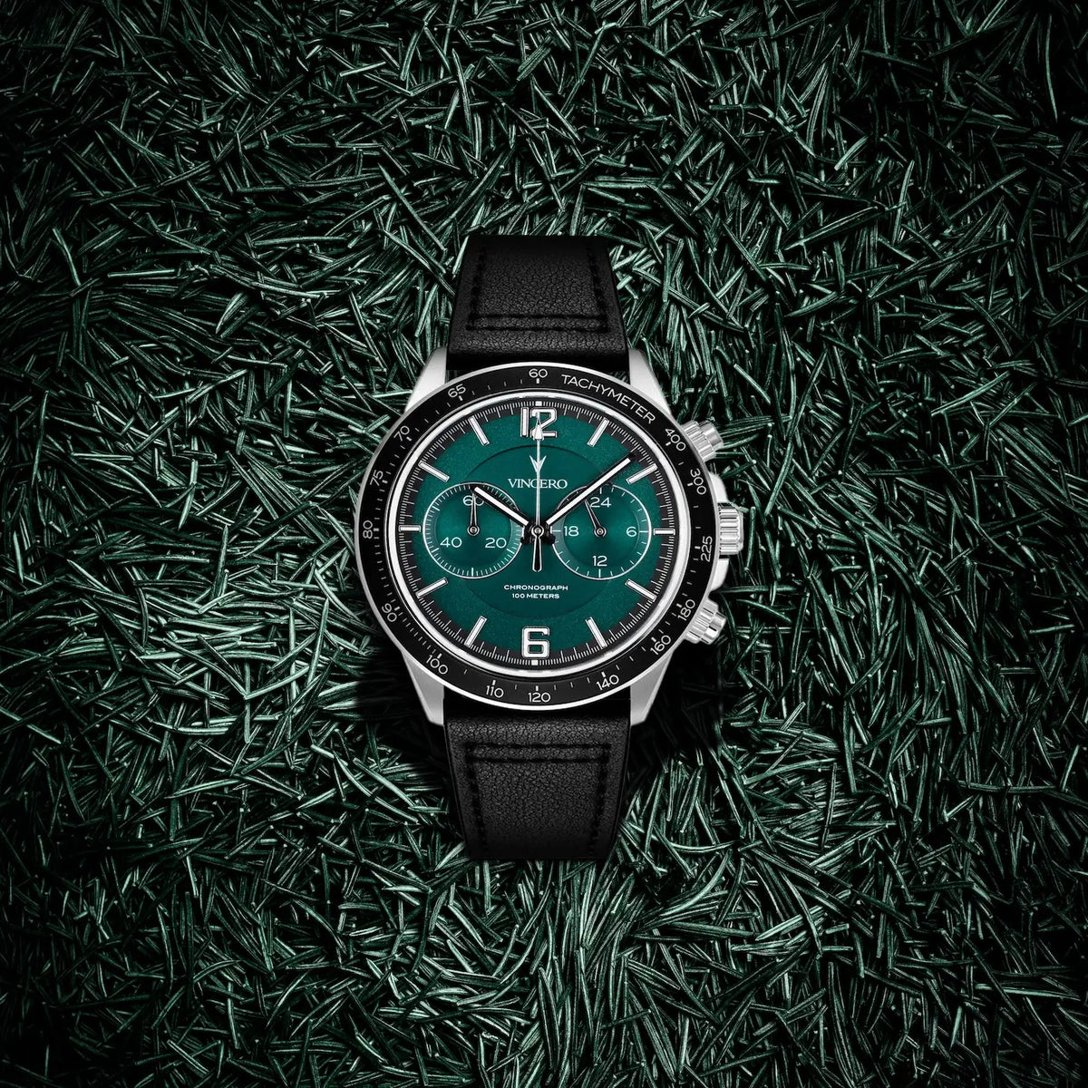 Watch with a green dial and black strap on a dark green grass-like background