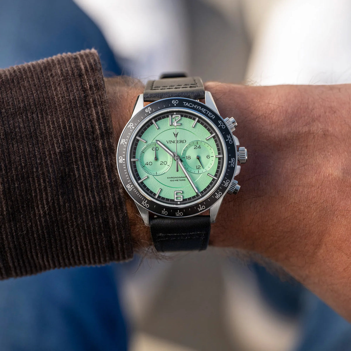 Close-up of a wrist wearing a watch with a green face and black strap.